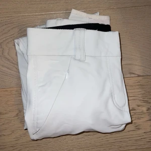 Vita ridbyxor med dragkedja - Snygga vita ridbyxor med dragkedja och bälteshällor. Perfekta för ridning med en stilren design och praktiska fickor. Passar bra för både träning och tävling.