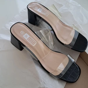 Svarta sandaler med klack från Lucky Shoes - Snygga svarta sandaler från Lucky Shoes med transparenta remmar och en fyrkantig tå. De har en stabil klack och en stilren design som passar perfekt för varmare dagar.