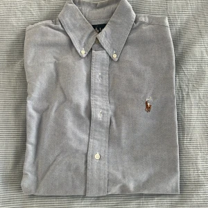 Ljusblå skjorta från Ralph Lauren - Säljer en stilren ljusblå skjorta från Ralph Lauren med broderad logotyp på bröstet. Skjortan har långa ärmar och knappar framtill samt på kragen. Perfekt för en klassisk look.