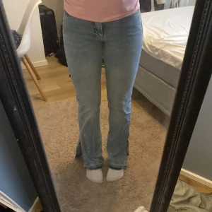 Blå jeans med slits - Säljer ett par blå jeans med slits vid bensluten. De har en klassisk design med en rak passform och är perfekta för en avslappnad stil. Jeansen har en snygg ljusblå färg och är tillverkade i denim. 