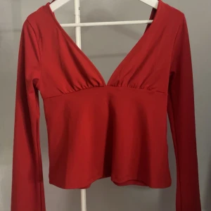 Röd långärmad topp med knyt - Snygg röd topp med långa ärmar och v-ringning. Toppen har en knytning i ryggen och utsvängda armar. Använd endast en gång och kommer tyvärr inte till mer användning🥰Bara att höra av dig om du vill ha bild med den på så fixar jag det! 