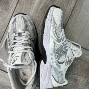 Vita och grå sneakers från New Balance - Snygga och bekväma vita och grå sneakers från New Balance med svart sula och snörning. Perfekta för en sportig look eller en avslappnad dag på stan.