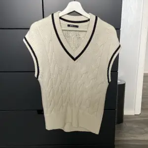 Säljer en stilren vit stickad väst från Gina Tricot med svarta detaljer. Västen har en v-ringad design och ett klassiskt flätmönster. Den är stor i storleken men är gjord för att vara lite baggy. Perfekt för lager-på-lager-stil. Väldigt skön och mjuk, håller även värmen bra! .