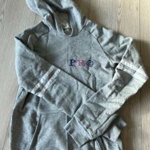 Grå hoodie med tryck - Säljer en grå hoodie med tryck i lila och rosa. Den har en stor ficka framtill och vita ränder på ärmarna. Perfekt för en avslappnad stil.🩷🩷