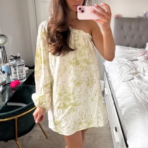 One Shoulder klänning!  - Säljer en söt vit klänning med grönt blommönster. Klänningen har en one-shoulder design och långa ärmar, perfekt för sommaren 