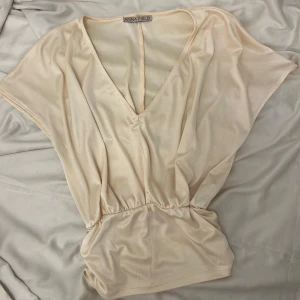 Ljusrosa blus från Anna Field - Säljer en elegant beige blus från Anna Field med v-ringning och korta ärmar. Blusen har en lös passform och är tillverkad i ett mjukt, syntetiskt material. Perfekt för en stilren look.