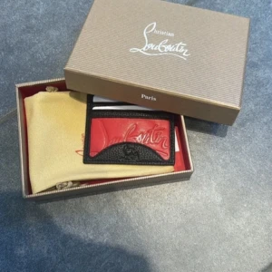Plånbok från Christian Louboutin - Snygg och stilren plånbok från Christian Louboutin i svart och rött skinn. Den har plats för flera kort och kommer i originalförpackning med dustbag och instruktioner. Perfekt för att hålla dina kort organiserade med stil.