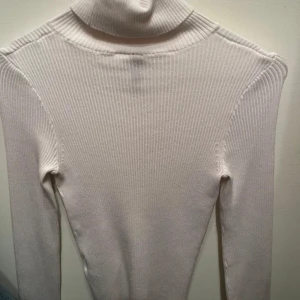 Vit ribbad polotröja från H&M Divided - Säljer en stilren vit ribbad polotröja från H&M Divided. Tröjan har en klassisk polokrage och långa ärmar, perfekt för kyligare dagar. Enkel att matcha med olika outfits.