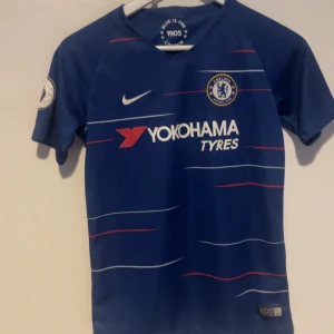 Blå Chelsea fotbollströja - Säljer en blå Chelsea fotbollströja från Nike med korta ärmar. Tröjan har röda och vita detaljer samt Yokohama Tyres som sponsorlogga. På baksidan finns namnet Hudson-Odoi och nummer 20.