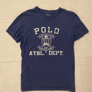 Blå t-shirt från Ralph Lauren - Säljer en blå t-shirt från Ralph Lauren med ett schysst tryck. Mycket bra skick. Slitna detaljer är design. Perfekt till våren/sommarn. Nypris runt 1000kr mitt pris 299kr.