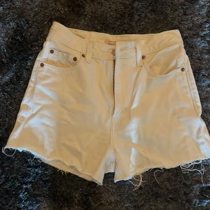Vita shorts från Levi's - Säljer ett par snygga vita shorts från Levi's med hög midja och fransiga kanter. De har en klassisk femficksdesign och knappgylf. Perfekta för sommardagar! 🌞(har klippt shortsen själv)