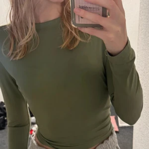 Olivgrön långärmad croppad topp - Säljer en olivgrön långärmad croppad topp med rund halsringning. Sitter tight och är perfekt att styla med både jeans och kjol. Enkel och stilren design utan mönster eller detaljer.