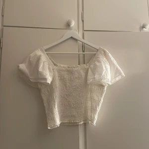 Vit blus från Kappahl - Säljer en söt vit blus från Kappahl med puffiga korta volang ärmar och smockad kropp. Perfekt till sommaren och enkel att matcha med både kjol och jeans. Superfin och luftig modell! Jag är en xs/s och den sitter lite lösare på mig men endå fint!