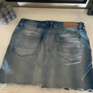 Blå jeanskjol med rå kant - Säljer en klassisk blå jeanskjol med fransig kant nertill och slitna detaljer. Kjolen har fickor både fram och bak samt dragkedja och knapp i midjan. Perfekt för en avslappnad och cool stil. Skicka gärna prisförslag🩷