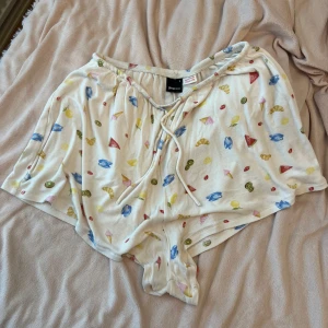 Vita shorts med godismönster och snörning - Supermjuka vita shorts från Monki med färgglatt godismönster i blått, rött, gult och grönt. Shortsen har lös passform, elastisk midja och snörning framtill. Perfekta för sommaren eller som mysplagg hemma.