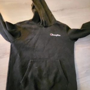Svart hoodie från Champion - Säljer en svart hoodie från Champion med klassisk logga på bröstet. Tröjan har huva och en stor magficka framtill. Perfekt för en avslappnad stil och enkel att matcha med det mesta. Tvättas självklart innan fraktning 