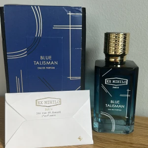 Blue Talisman Eau de Parfum från Ex Nihilo - Lyxig parfym från Ex Nihilo, Blue Talisman, i en elegant blå glasflaska med guldigt lock och geometriska detaljer. Kommer med originalförpackning och ett exklusivt kuvert från butiken i Paris.