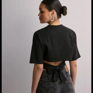 Nelly töja med knyt bak  - Säljer en svart croppad topp med korta ärmar och snygg knytning i ryggen. Perfekt för att skapa en trendig och stilren look. Toppen har en boxig passform och är lätt att matcha med olika outfits. Skriv om ni vill ha fler detaljer eller bilder 