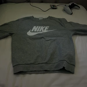 Grå sweatshirt från Nike - Säljer en grå sweatshirt från Nike med stor vit logga på bröstet. Tröjan har rund halsringning och långa ärmar med ribbade muddar. Perfekt för en sportig och avslappnad stil. Pris kan diskuteras hör av dig bara! MVH, Lukas