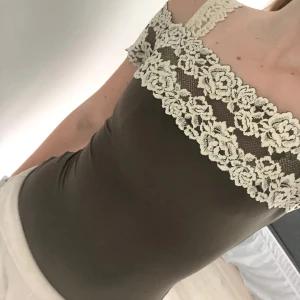 Brun bodysuit med spetsdetaljer från Intimissimi - Supersnygg brun bodysuit från Intimissimi med breda axelband och vacker cremefärgad spets upptill. Stretchigt material som sitter tight och markerar figuren. Perfekt att styla med jeans eller kjol. Är i storlek S!