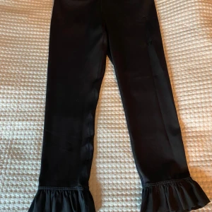 Svarta leggings med volang - Svarta träningstights med snygga volangdetaljer längst ner vid bensluten. Tillverkade i stretchigt material med 73% polyester och 27% spandex för en bekväm passform. Perfekta för dig som vill ha något extra till din outfit. 