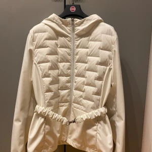 Vit quiltad jacka med huva från Colmar - Säljer en  vit jacka från Colmar i gott skick med quiltade partier framtill och baktill. Jackan är ofodrad, har huva, dragkedja framtill och markerad midja med resår. Italiens 42 som motsvara stl 36. Perfekt för dig som vill ha en stilren och sportig look.