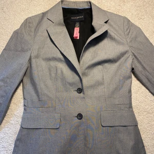 Banana Republic Kavaj - Snygg grå kavaj från Banana Republic med klassisk krage och två knappar framtill. Kavajen har två fickor med lock och är tillverkad i bomull med lite stretch för extra komfort. Perfekt för en stilren look. Har en liten fläck på höger axel som knappt syns. Kom privat för fler frågor 💕