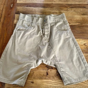 Beiga shorts från HUMÖR - Snygga beiga shorts från HUMÖR med normal passform. De har klassisk femficksdesign, bälteshällor och stängs med dragkedja och knapp. Materialet är en mix av polyester och bomull, vilket gör dem både slitstarka och bekväma.