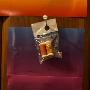 Örhängen med apelsinjuicekartonger - Unika örhängen formade som små apelsinjuicekartonger i orange och vitt. Perfekt accessoar för dig som vill sticka ut med något lekfullt och färgglatt. Säljs i förpackning med krok i guldton.