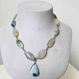 Halsband med stora stenar i blå och beige toner - Unikt halsband med stora, oregelbundna stenar i blå, beige och vita nyanser. Stenarna har vackra naturliga mönster och är sammanlänkade med silverfärgade metallringar. Perfekt för dig som vill sticka ut med ett färgstarkt smycke. Okej vintage skick