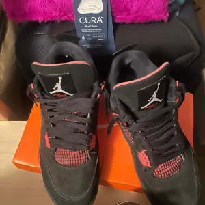 Jordan 4 Red thunders  - Säljer ett par svarta Nike Air Jordans med röda detaljer och svart snörning. Skorna har en klassisk siluett med meshpaneler och Jumpman-logga på plösen. Perfekta för dig som gillar streetwear och sneakers med attityd.