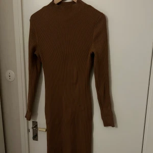 Brun ribbad långklänning - Säljer en brun ribbad långklänning med lång ärm och hög hals. Materialet är mjukt och stretchigt, vilket gör den både bekväm och stilren.
