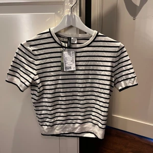 Vit och svart randig topp från H&M - Kortärmad topp från H&M i vit med svarta horisontella ränder. Rund halsringning och ribbad kant nedtill. Perfekt för en stilren och enkel look.