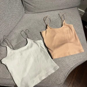 Ribbad linnetopp från 157 - Två ribbade linnetoppar från 157 i färgerna beige och vit. Båda har tunna axelband och croppad passform, perfekta för varma dagar. Säljes tillsammans eller separat!