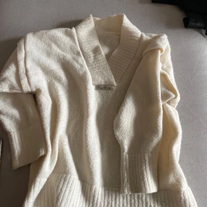 Vit stickad kofta från Twinlove - Mysig vit stickad kofta från Twinlove med bred ribbad krage och muddar. Koftan har en dekorativ metallbricka vid halsen och är perfekt för lager-på-lager. Långärmad och med bred ribbstickning nedtill.