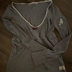 Grå ribbad långärmad tröja från Odd Molly - Supersöt grå ribbad tröja från Odd Molly med v-ringning, spetskant och liten rosett framtill. Broderad detalj på ena ärmen. Perfekt för lager-på-lager och snygg till jeans eller kjol. Använd fåtal gånger så den är i väldigt fint skick 🤩💕
