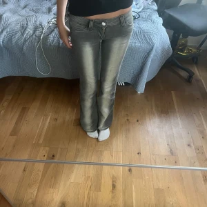 Grå bootcut jeans - Säljer ett par grå bootcut jeans med klassisk femficksdesign och knappgylf. Jeansen har en lätt tvättad look och raka ben som blir vidare nedtill. Perfekta för dig som gillar en retrostil.