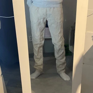 Beiga linnebyxor med normal passform - Säljer ett par beiga linnebyxor med normal passform.       100% Linne. Passar dig som är mellan 175-180 cm. Byxorna har klassisk rak design, sidofickor och knappdetalj vid bakfickan. Perfekta för en avslappnad och stilren look under varmare dagar. Går även och sätta dit ett bälte och knyta! Hör av dig vid minsta fundering!