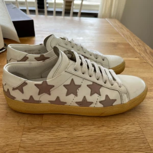 Saint Laurent sneakers med stjärnor - Säljer ett par väldigt fina vita Saint Laurent sneakers med rosa skärnmönster. Perfekta att ha nu i sommar! Skorna är i bra skick och i storlek 37! Hör av er vid intresse!!//FR