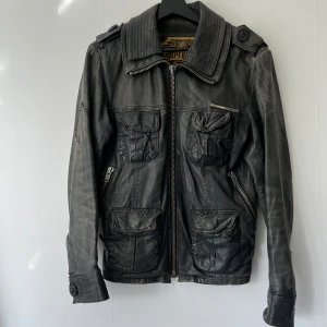 Skinnjacka - Säljer en skinnjacka från Superdry! Storlek S. Tyvärr har hängaren på dragkedjan lossnat men den går fortfarande stänga. Jackan har också en liten skada vid armbåge (se bild) 
