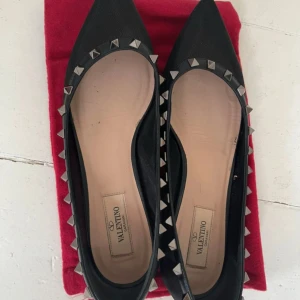 Svarta Valentino Rockstud ballerinaskor - Svarta ballerinaskor från Valentino med spetsig tå och ikoniska Rockstud-nitar runt kanten. Skorna har platt sula. Perfekta för dig som vill ha en edgy men stilren look. Skriv för fler bilder eller frågor!😊