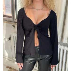 Svart långärmad topp med knyt framtill - Trendig svart långärmad topp med knytning framtill ifrån Design by Si, storlek S/M