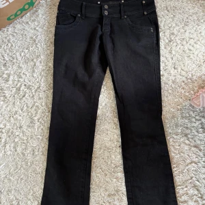 Svarta jeansbyxor från Gina Tricot - Svarta jeansbyxor från Gina Tricot med klassisk femficksdesign och raka ben. Byxorna har dubbla knappar i midjan och diskreta nitar vid fickorna. Perfekta för en stilren och enkel look. Visar tidigare är det jeans som köpta på Sellpy men det syns verkligen inte att de är begbegagnade!