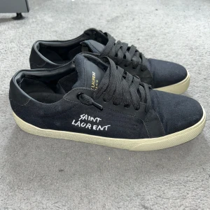 Saint Laurent sneakers - Svarta sneakers från Saint Laurent i storlek 43 men passar även 42. Skorna har en vit sula och broderad logga på sidan. Klassisk snörning framtill och diskret Saint Laurent Paris-tryck på plösen. Box, dustbag och authentic card medföljer. Bara höra av dig vid frågor eller funderingar! 