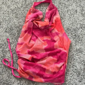 Somrig rosa och orange halterneckklänning - Säljer en snygg halterneckklänning i rosa och orange toner med draperad framsida och knyt i sidan. Klänningen har ett unikt mönster och är perfekt för sommardagar. Materialet känns lätt och luftigt. Perfekt för sommaren❤️
