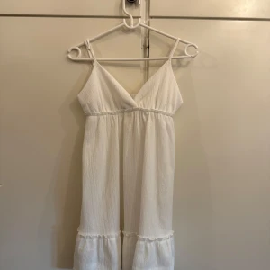 Vit sommarklänning från Divided Hm - Säljer en vit ärmlös klänning från Divided i storlek S. Klänningen har smala axelband, v-ringning och volangdetalj nertill. Perfekt för varma dagar och enkel att styla med sandaler eller sneakers.