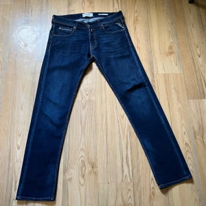 Mörkblå jeans Replay Grover - Säljer ett par mörkblå Replay Grover jeans med raka ben och klassisk femficksdesign. Jeansen har snygga kontrastsömmar och en liten Replay-logga vid fickan. Passar perfekt till dig som gillar en tidlös och stilren look.