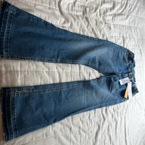 Blå bootcut jeans från Gina Tricot - Säljer ett par blå bootcut jeans från Gina Tricot i storlek 158. Jeansen har råa, fransiga benslut och klassisk femficksdesign. De är tillverkade i denim och har normal passform med dragkedja och knapp framtill. Och har även slits på båda benen, dem är aldrig använda💞