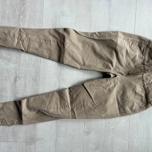 Beige ridbyxor från Pikeur - Snygga beige ridbyxor från Pikeur med två knappar i midjan och klassiska fickor framtill. Byxorna har en figurnära passform och är perfekta för ridning. Materialet känns mjukt och stretchigt för extra komfort.