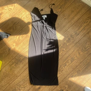 Svart långklänning med knyt - Säljer en svart långklänning med smala axelband och snygg knytning framtill. Klänningen har en elegant v-ringning och är figurnära i modellen. Perfekt för dig som gillar stilrena och klassiska plagg.